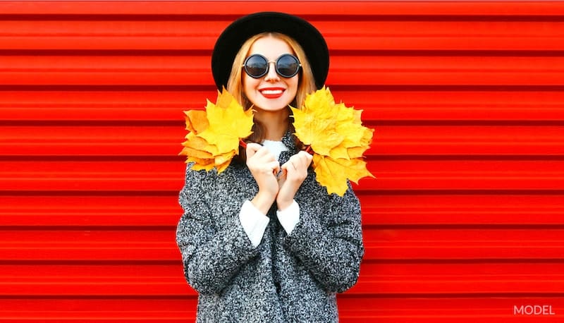 Happy woman holding fall leaves in front of a red backdrop